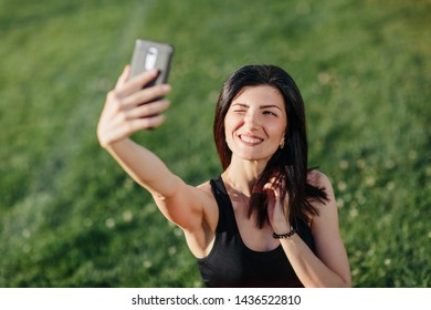 young beautiful sport brunette girl in sports clothes sit on the grass after a workout and making selfie on a smart phone. Healthy lifestyle concept. - Shutterstock ID 1436522810