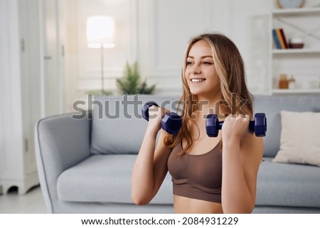 The young beautiful sports girl in leggings and a top does exercises with dumbells. Healthy lifestyle. A woman goes in for sports at home while using laptop.