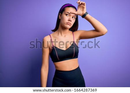 Young beautiful sporty girl doing sport wearing sportswear over isolated purple background making fun of people with fingers on forehead doing loser gesture mocking and insulting.