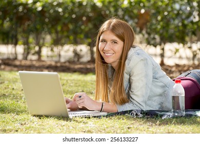 young beautiful student girl lying on park grass with computer laptop on rug studying happy preparing exam or surfing on internet in technology and education concept