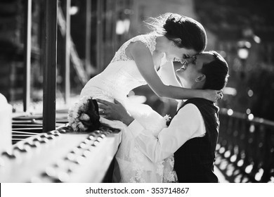 Young Beautiful Stylish Fun Pair Of Newlyweds On A Bridge In Budapest, Hungary. Beautiful Woman In A White Wedding Dress And Handsome Man In The Three-piece Suit.