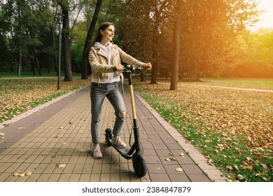 Young beautiful stylish woman riding electric scooter by autumn park, ecological transport - Powered by Shutterstock