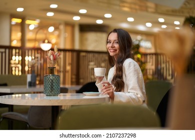 Young beautiful stylish woman in white blazer with cup od coffee sitting in restaurant - Shutterstock ID 2107237298