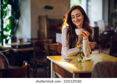 Young beautiful stylish woman in white blazer with cup of coffee sitting in cafe. Copy space. Gorgeous female drinking hot beverage and sitting indoor in an urban cafeteria. Waiting for her friends. - Powered by Shutterstock