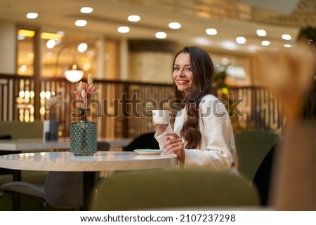 Young beautiful stylish woman in white blazer with cup od coffee sitting in restaurant