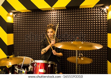young beautiful tattooed girl in a leather jacket plays drums in a recording Studio on the bright black and yellow band.