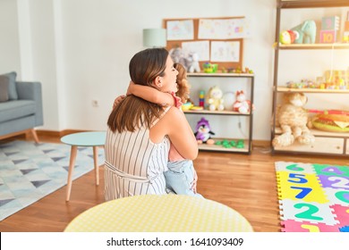 Young beautiful teacher and blond toddler girl hugging at kindergarten