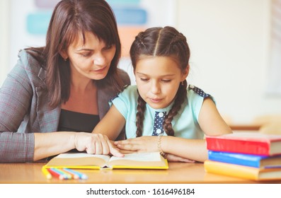 Young Beautiful Teacher With Schoolgirl Reading Book At School In The Classroom