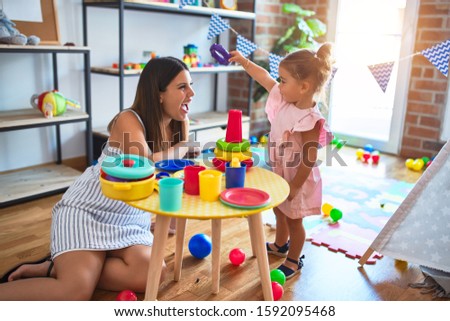 Young beautiful teacher and toddler building pyramid using hoops on the table at kindergarten