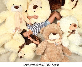Young beautiful teenage girl lying with many teddy bears soft toys happy smiling and looking up at home warm color carpet
