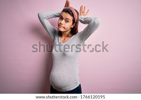 Young beautiful teenager girl pregnant expecting baby over isolated pink background Doing bunny ears gesture with hands palms looking cynical and skeptical. Easter rabbit concept.