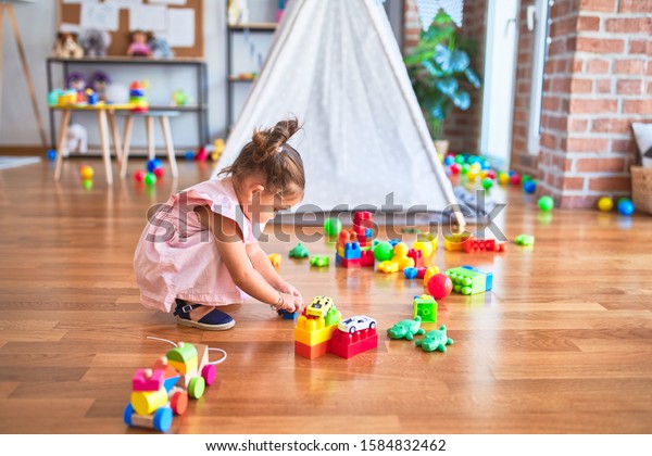 Young beautiful toddler sitting on the\
floor playing with small cars toys at\
kindergaten