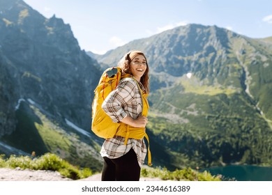 Young beautiful tourist woman with curly hair on top of a mountain. Active woman enjoys the beautiful scenery of the majestic mountains. Travel, adventure. Concept of an active lifestyle. - Powered by Shutterstock