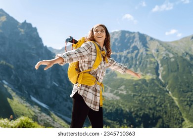Young beautiful tourist woman with curly hair on top of a mountain. Active woman enjoys the beautiful scenery of the majestic mountains. Travel, adventure. Concept of an active lifestyle. - Shutterstock ID 2345710363