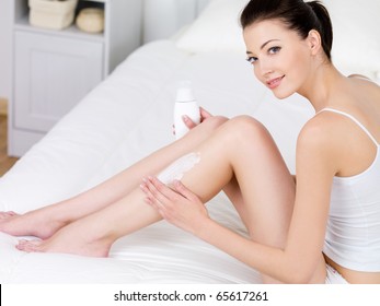 Young Beautiful Woman Applying Body Lotion On Her Attractive Legs - Indoors