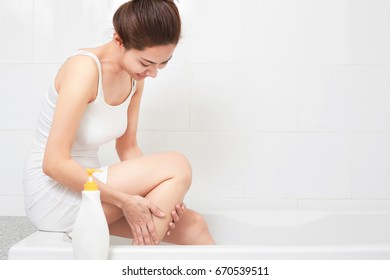 Young Beautiful Woman Applying Body Lotion On Her Attractive Legs In Bathroom.