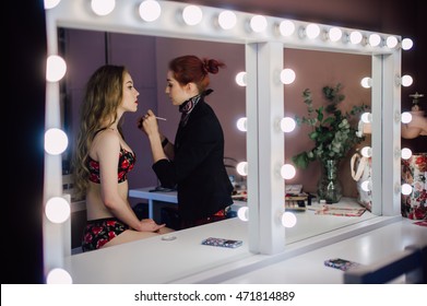 Young Beautiful Woman Applying Her Make Up Face With Brush, Looking In A Mirror, Sitting On Chair At Dressing Room With Vintage Mirror Dark Room