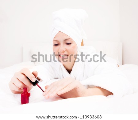 young beautiful woman applying red nail polish in bed at home