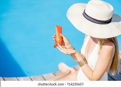 Young beautiful woman applying sunscreen lotion sitting on the wooden poolside. Sunscreen solar cream uv protection concept - Powered by Shutterstock