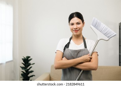 Young beautiful woman with apron and rubber glove ready for cleaning home background. Housekeeping housework or maid worker holding broom