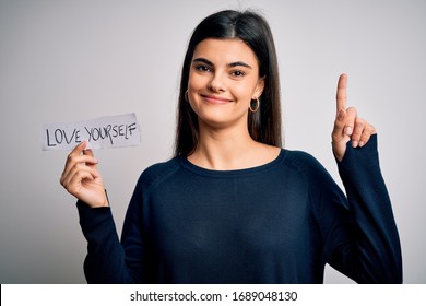 Young Beautiful Woman Asking For Take Care Of You Holding Paper With Love Yourself Message Surprised With An Idea Or Question Pointing Finger With Happy Face, Number One