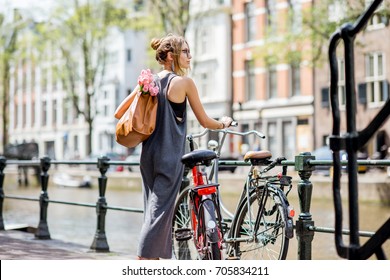 Young and beautiful woman with bag and flowers walking with bicycle on the water channel in Amsterdam city