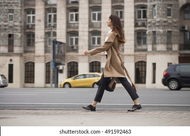Young beautiful woman in beige coat with a bag walking on the autumn street