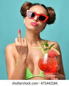 Young beautiful woman in bikini hold red margarita tropical cocktail juice and show middle finger fuck you off sign in fashion sunglasses on blue mint background