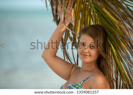 Young beautiful woman in bikini under palm tree on sea background