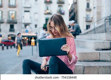 Young Beautiful Woman With Blonde Hair Takes Laptop In Protective Plastic Mockup Cover Out Of Fashion Leather Bag. Student Sits On Stairs Or Steps Of University Building, Hipster Freelance Lifestyle