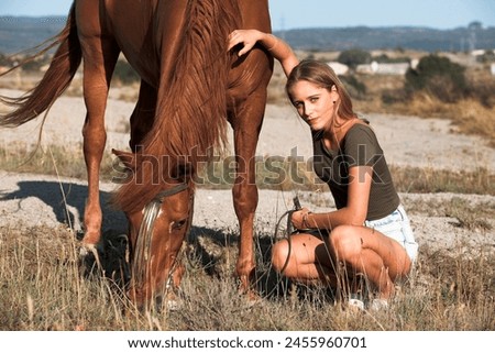 Young beautiful woman with blue eyes posing with her horse at mountain during sunset.