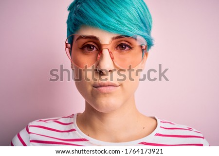 Young beautiful woman with blue fashion hair wearing fanny glasses with hearts with a confident expression on smart face thinking serious