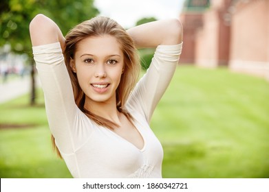Junge schöne Frau in einem hellen Kleid auf einem Hintergrund aus getrimmtem grünem Rasen und roten Wänden.