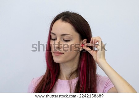 A young, beautiful woman with bright hair inserts earplugs to protect against loud noise