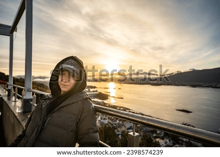 young beautiful woman in cap looking at camera with mountains on background during sunrise in alesund, norway