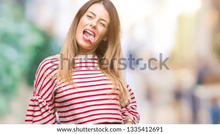 Young beautiful woman casual stripes winter sweater over isolated background sticking tongue out happy with funny expression. Emotion concept.