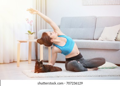 Young Beautiful Woman With Cat Practicing Yoga Pose At Home