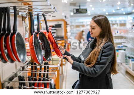 young beautiful woman choosing frying pan utensil dishes in a store supermarket shop.