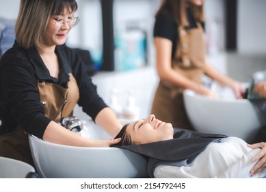 young beautiful woman client getting hair treatment in beauty salon with professional female stylist hairdresser, using shampoo and water on person head to clean and coiffure hair fashion service
