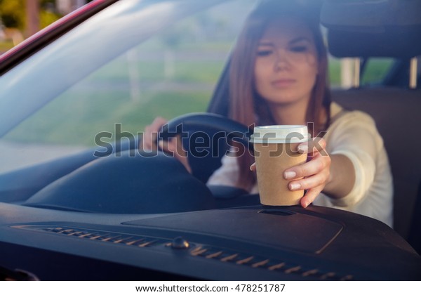 Young, beautiful woman with coffee\
in hand behind the wheel of a car. Don\'t sleep and\
drive
