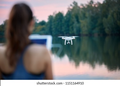 Young beautiful woman controls a white quadcopter by remote controller with a tablet. Focused on the drone, the pilot is out of focus. Teaching flying with a drone in summer nature.  - Powered by Shutterstock