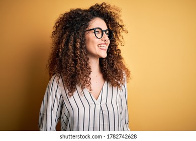 Young beautiful woman with curly hair and piercing wearing striped shirt and glasses looking away to side with smile on face, natural expression. Laughing confident. - Powered by Shutterstock