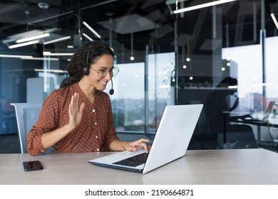 Young beautiful woman curly hair using laptop and laptop for online meeting video call, Arab business woman working inside office building, female employee cheerfully waving hand, greeting gesture - Shutterstock ID 2190664871