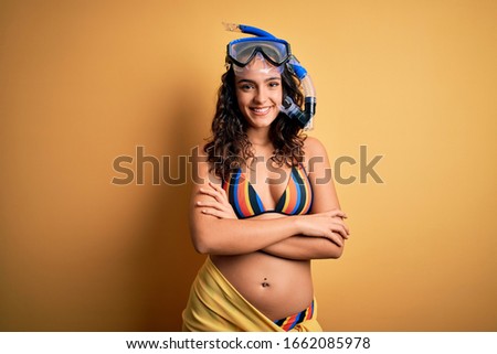 Young beautiful woman with curly hair on vacation wearing bikini and diving googles happy face smiling with crossed arms looking at the camera. Positive person.