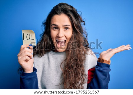 Young beautiful woman with curly hair holding reminder paper with lol message very happy and excited, winner expression celebrating victory screaming with big smile and raised hands