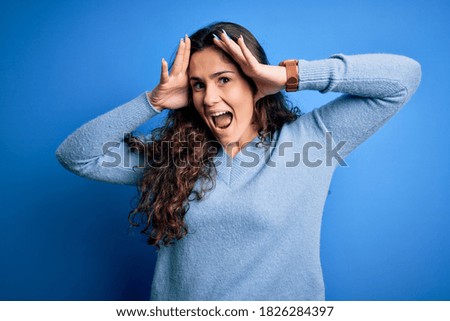 Young beautiful woman with curly hair wearing blue casual sweater over isolated background Smiling cheerful playing peek a boo with hands showing face. Surprised and exited