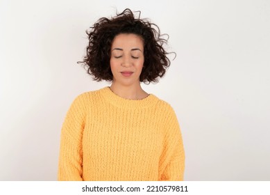 young beautiful woman with curly short hair wearing yellow sweater over white wall nice-looking sweet charming cute attractive lovely winsome sweet peaceful closed eyes