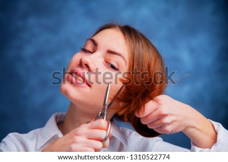 Young beautiful woman cutting with shears her long hair. Hair care concept. Studio photo shoot.