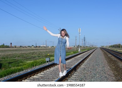 Young beautiful woman in a denim dress walks on railroad. Keeps balance with hands. - Shutterstock ID 1988554187