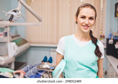 Young Beautiful Woman Dentist Smile Cheerfully When Holding Full Face Protection Shield Standing In Her Office In Front Of Dental Chair With Patient. Copy Space